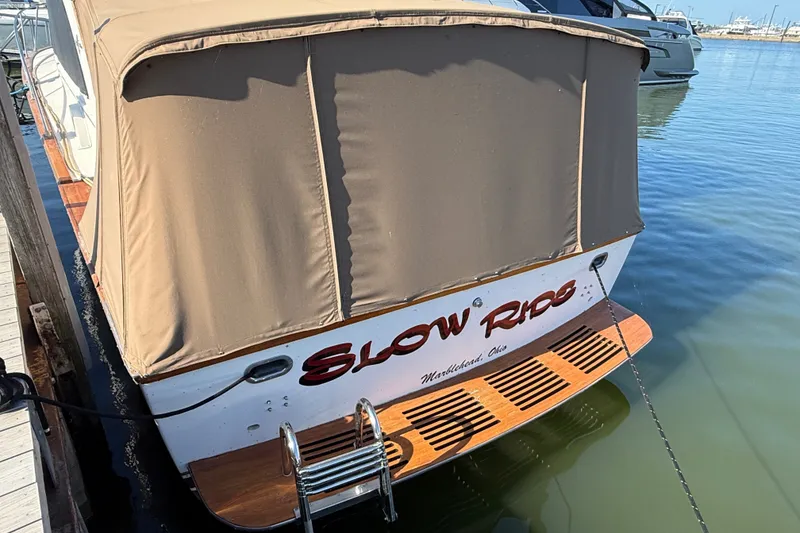 Slide: The Image of 1984 Egg Harbor 40 Sedan boat docked, featuring a beige cover and wooden swim platform. - 6