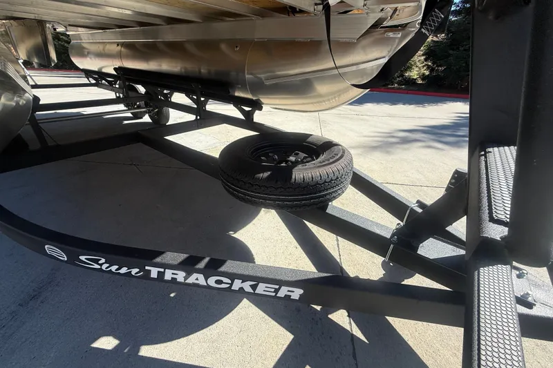 Slide: The Image of 2027 Sun Tracker SportFish 20 DLX trailer with spare tire, parked on concrete. - 53