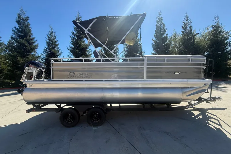 The Image of 2027 Sun Tracker SportFish 20 DLX pontoon boat on trailer, parked outdoors. - 0