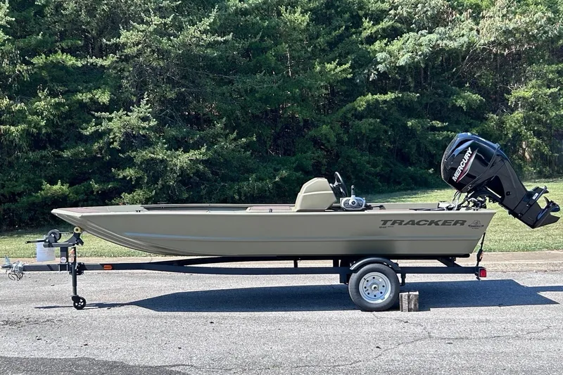 The Image of The image shows a Tracker Grizzly 1648 SC boat on a trailer, surrounded by trees. - 0
