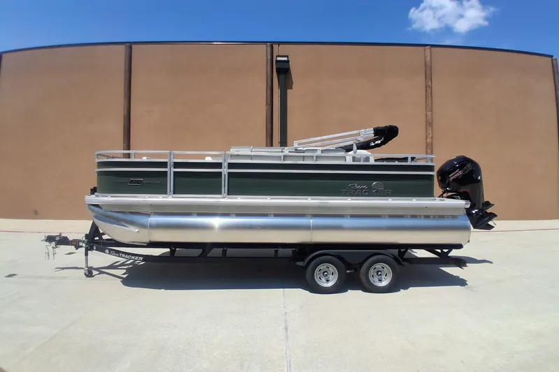 The Image of 2027 Sun Tracker Fishin' Barge 20 DLX pontoon boat on trailer, parked outdoors. - 0