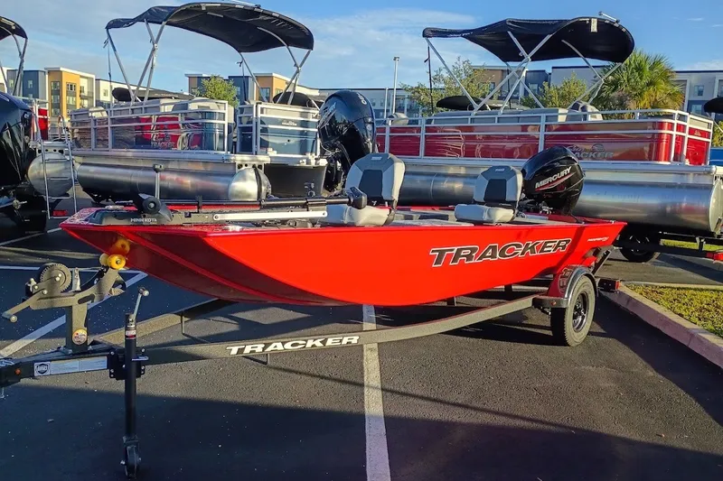 The Image of Red 2027 Tracker Panfish 17 boat on trailer, parked near pontoon boats. - 0