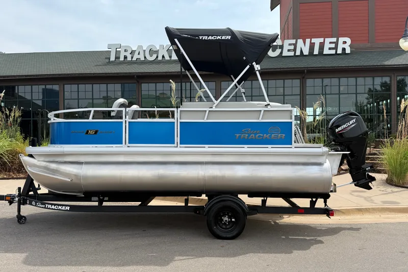 The Image of 2027 Sun Tracker Bass Buggy 16 XL Select pontoon boat on trailer outside showroom. - 0