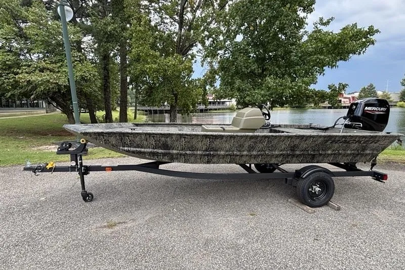 The Image of 2027 Tracker Grizzly 1648 SC boat on trailer, parked near a lake with trees. - 0