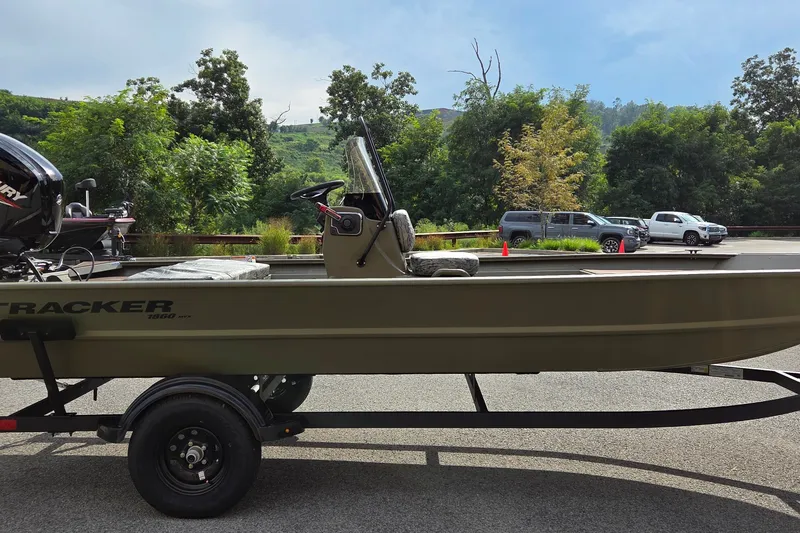 The Image of 2027 Tracker Grizzly 1860 CC boat on trailer, parked outdoors with trees in background. - 0