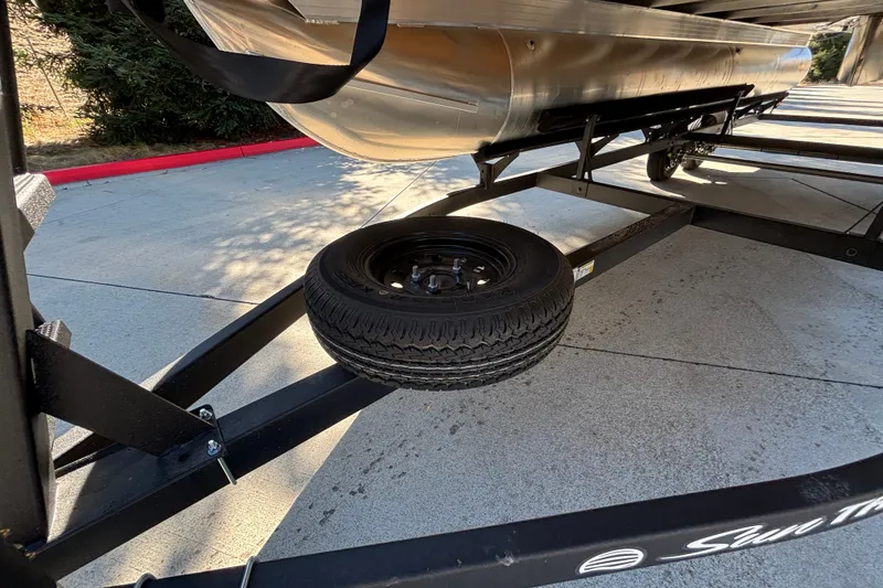 Slide: The Image of 2027 Sun Tracker SportFish 22 DLX trailer with spare tire on concrete surface. - 65