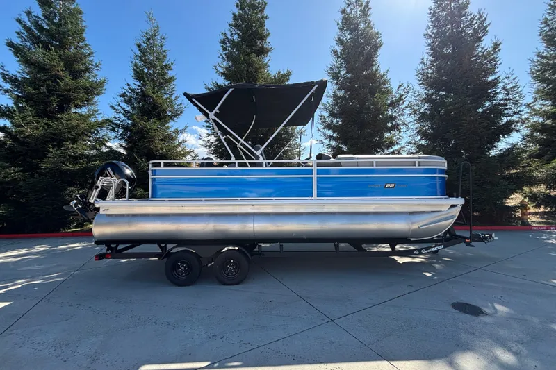 The Image of 2027 Sun Tracker SportFish 22 DLX pontoon boat on trailer, parked outdoors. - 0
