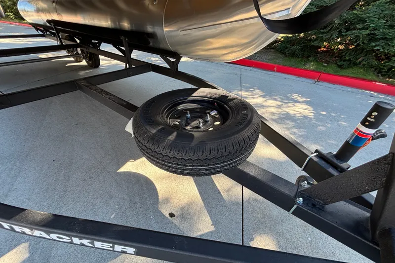 Slide: The Image of 2027 Sun Tracker SportFish 22 DLX trailer with spare tire on concrete surface. - 59
