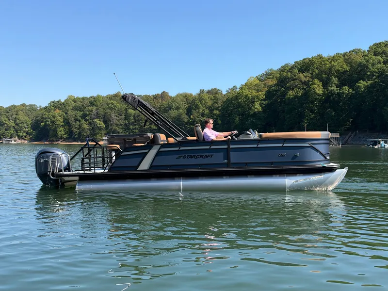 Slide: The Image of A 2027 Starcraft EXS 3 DL pontoon boat on a calm lake with a wooded shoreline. - 48
