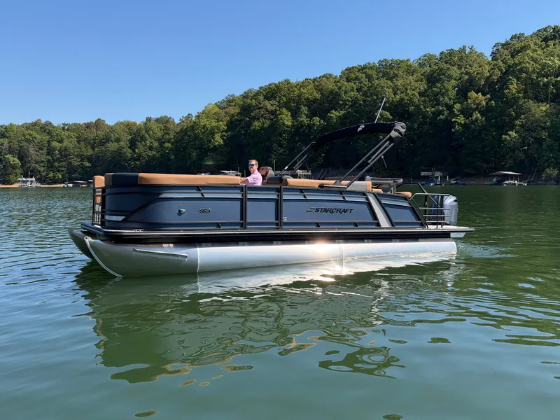 Slide: The Image of A 2027 Starcraft EXS 3 DL pontoon boat on a calm lake with a wooded shoreline. - 35