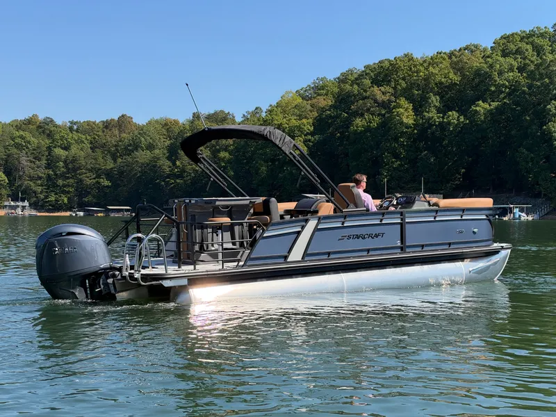 Slide: The Image of The image shows a 2027 Starcraft EXS 3 DL pontoon boat on a calm lake. - 46