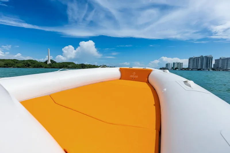 Slide: The Image of Modern Antudo 23 boat with orange seating, cruising on a sunny day near coastal buildings. - 5
