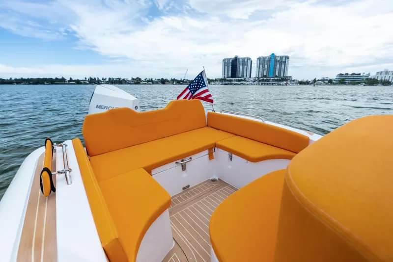 Slide: The Image of Modern Antudo 23 boat with orange seating, American flag, and cityscape view, 2025 model. - 1