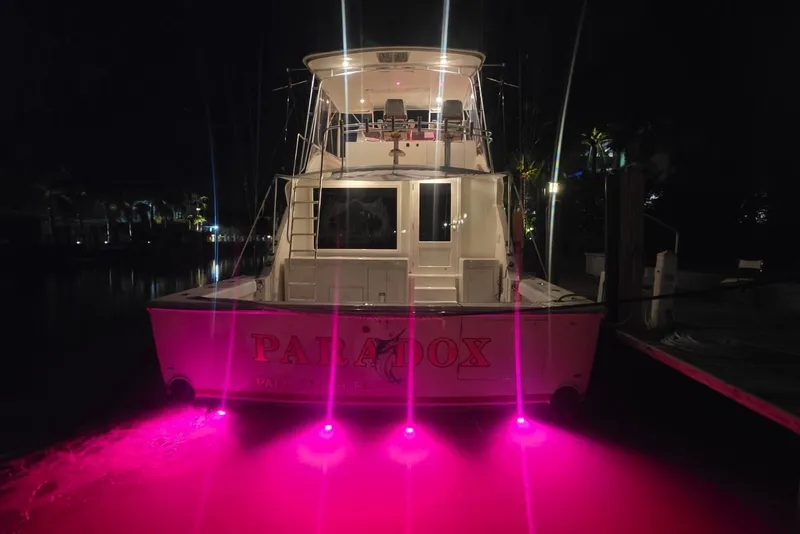 Slide: The Image of 1984 Bertram 54 Convertible yacht with pink underwater lights at night. - 51