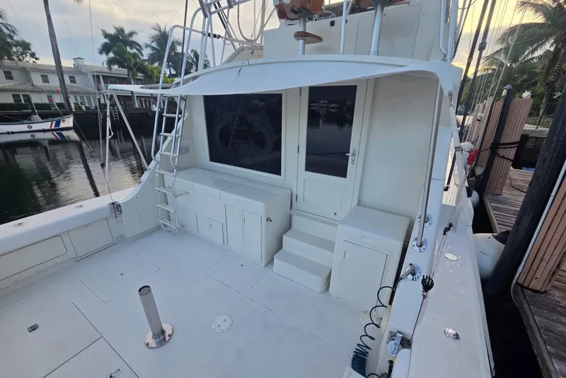 Slide: The Image of 1984 Bertram 54 Convertible yacht deck with ladder and storage, docked by palm trees. - 50