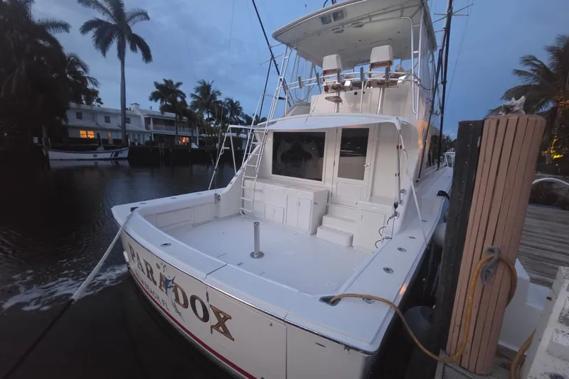 Slide: The Image of 1984 Bertram 54 Convertible yacht docked at marina, surrounded by palm trees. - 87