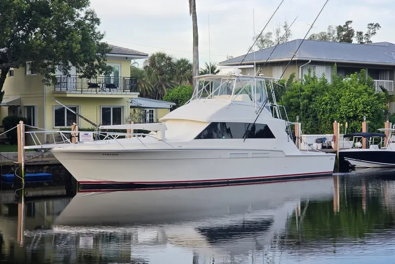 Slide: The Image of 1984 Bertram 54 Convertible yacht docked by waterfront homes, reflecting on calm water. - 23