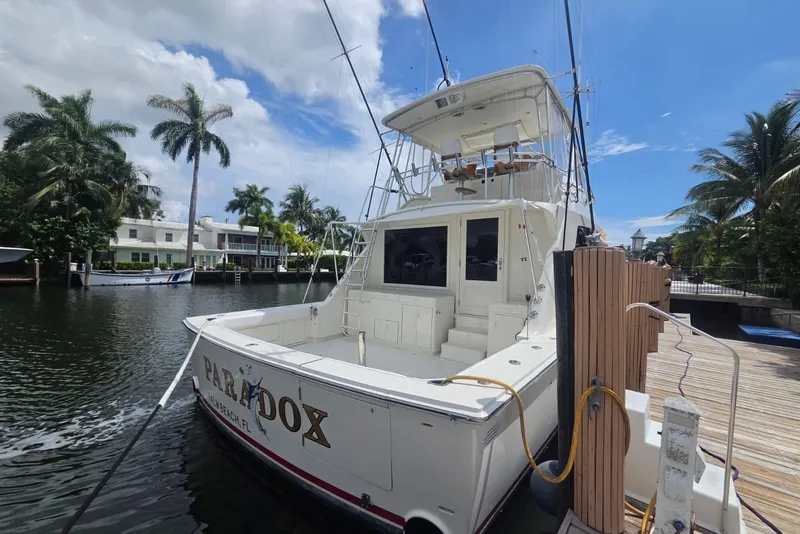 Slide: The Image of 1984 Bertram 54 Convertible yacht docked by palm trees under a blue sky. - 115