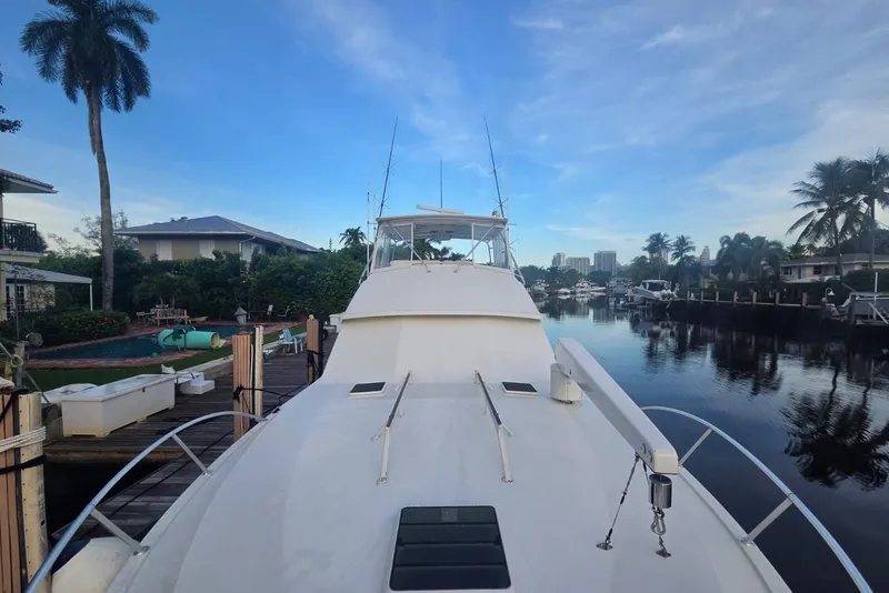 Slide: The Image of 1984 Bertram 54 Convertible yacht docked in a serene canal setting with palm trees. - 34