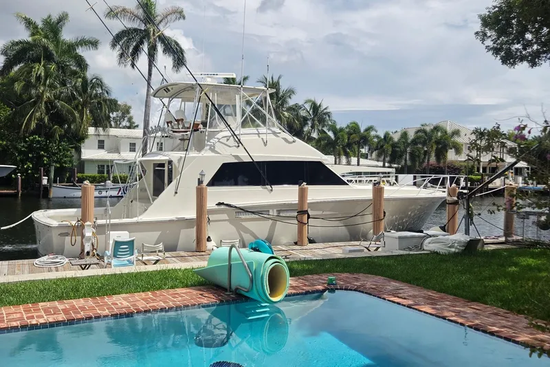 Slide: The Image of 1984 Bertram 54 Convertible yacht docked by a pool, surrounded by palm trees. - 111