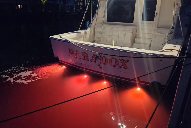 Slide: The Image of 1984 Bertram 54 Convertible boat with red underwater lights at night, docked in Palm Beach. - 79