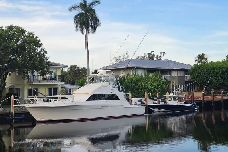 Slide: The Image of 1984 Bertram 54 Convertible yacht docked by waterfront homes, surrounded by lush greenery. - 22