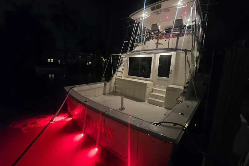 Slide: The Image of 1984 Bertram 54 Convertible yacht with red underwater lights at night. - 56