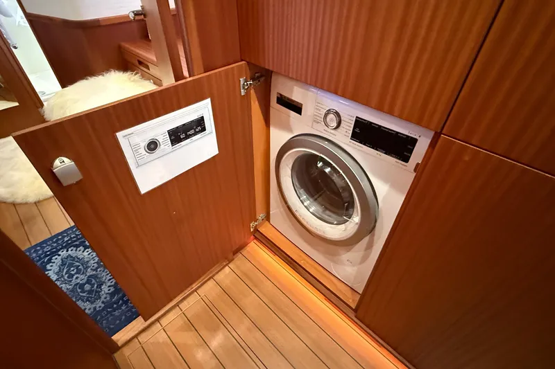 Slide: The Image of Laundry area with a washing machine inside a 2021 Elling E6 yacht's wooden cabinet. - 56