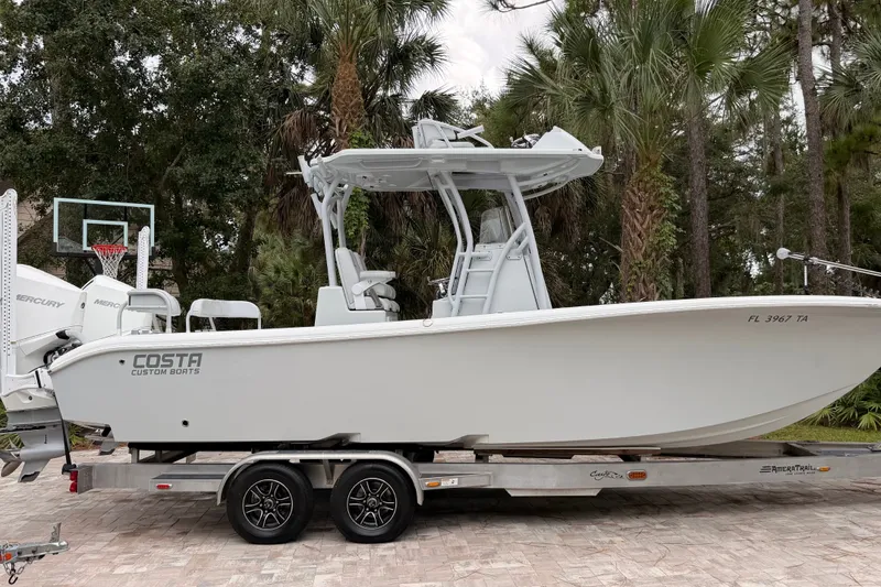 Slide: The Image of 2021 Costa Custom Boats 264HC on trailer, surrounded by trees and a basketball hoop. - 3