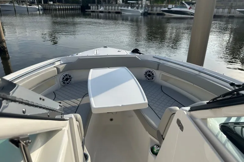 Slide: The Image of 2025 Pursuit DC 266 Dual Console boat interior with seating and table, docked by the water. - 10
