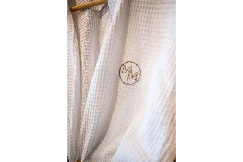 Slide: The Image of White waffle-textured robe with embroidered initials, hanging on a wooden hanger. - 139