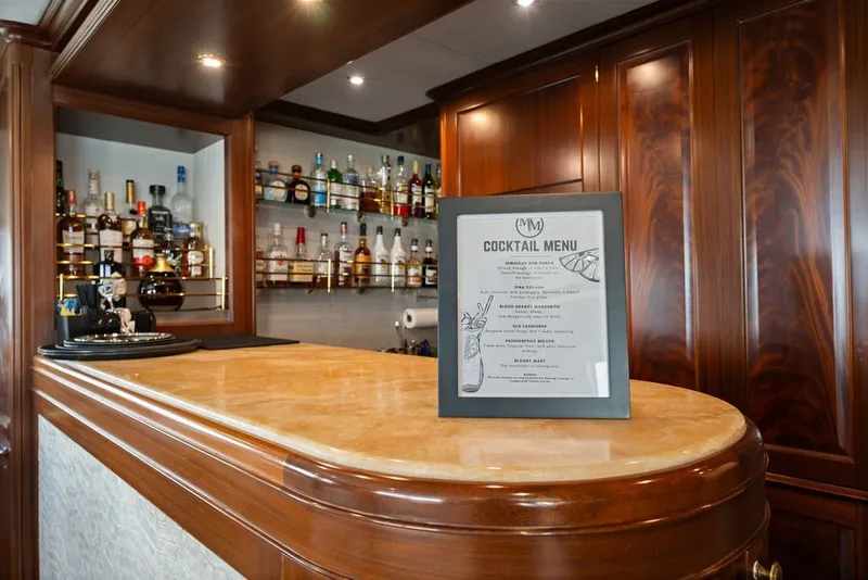 Slide: The Image of Luxurious yacht bar with cocktail menu, featuring elegant wood finishes on a 2007 Benetti 120 Classic. - 85