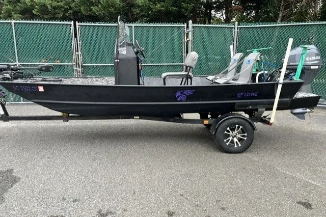 The Image of 1995 Lowe L1648 Jon boat on trailer, parked near green fence. - 1