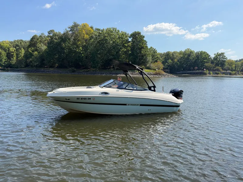 Slide: The Image of A 2021 Stingray 214 LR boat on a calm lake with a wooded shoreline in the background. - 0