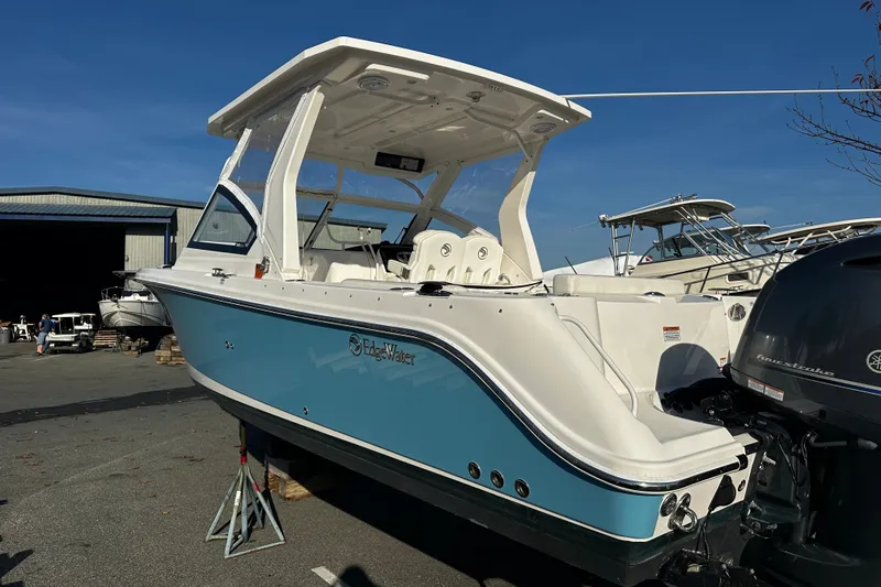 Slide: The Image of 2023 Edgewater 262CX Crossover boat with blue hull, docked outdoors under clear sky. - 3