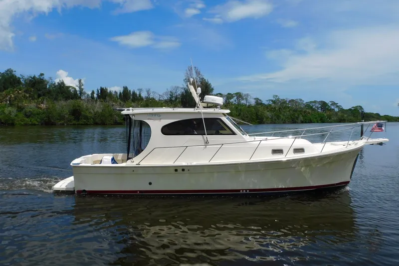 Slide: The Image of 2004 Mainship Pilot 30 Rum Runner cruising on a serene river under a clear blue sky. - 2