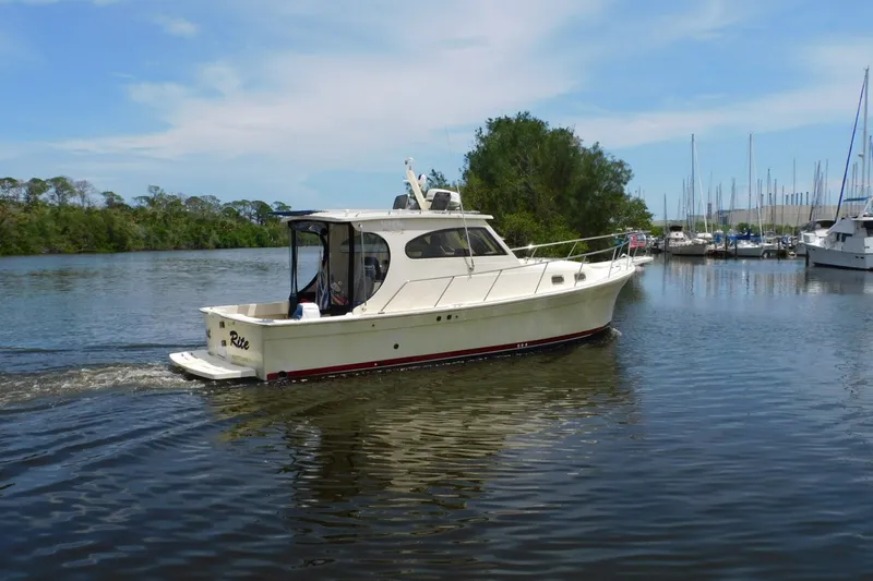 Slide: The Image of 2004 Mainship Pilot 30 Rum Runner cruising on a calm river near a marina. - 4