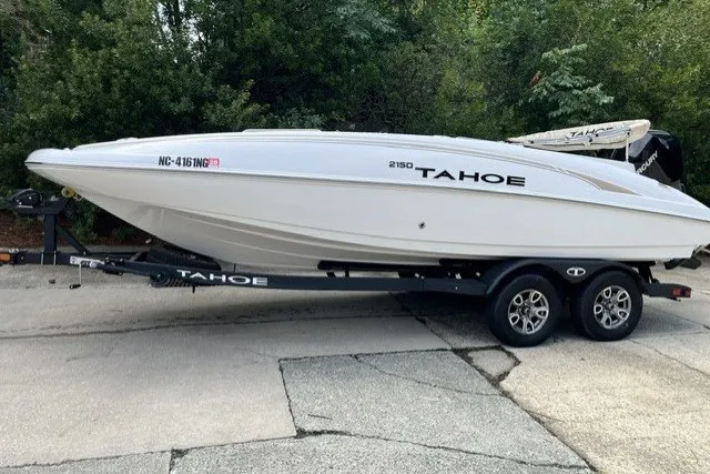 The Image of 2025 Tahoe 2150 boat on trailer, parked outdoors with lush greenery background. - 0