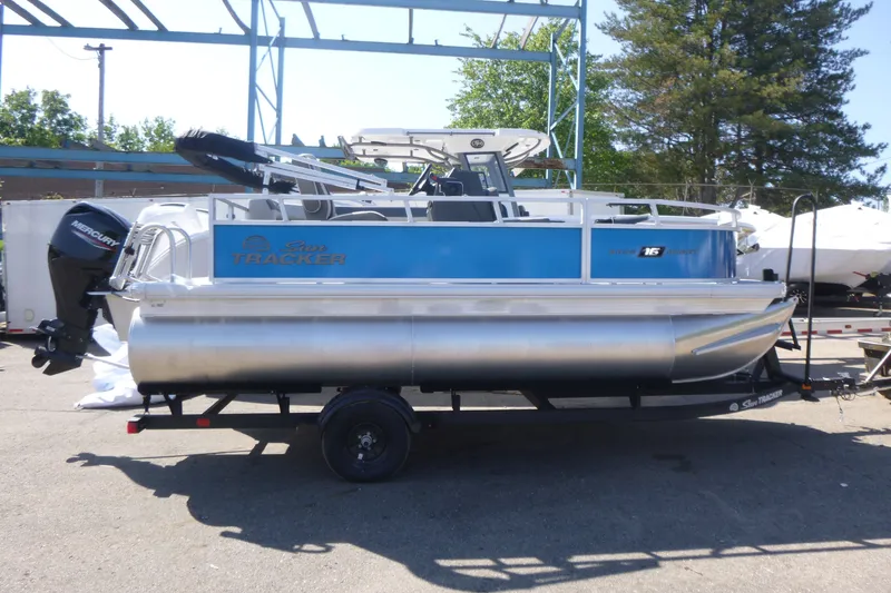 The Image of 2027 Sun Tracker Bass Buggy 16 XL Select pontoon boat on trailer, outdoors. - 1