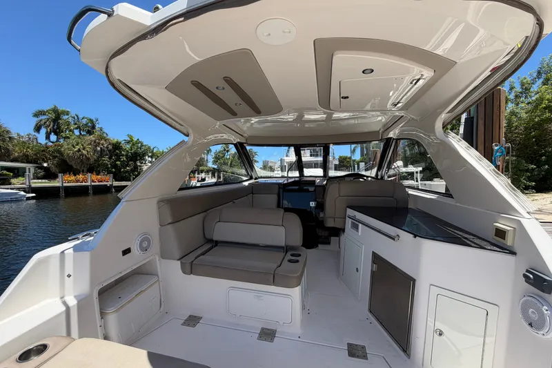 Slide: The Image of 2015 Regal 35 Sport Coupe interior with seating and kitchenette, docked by a scenic waterfront. - 18