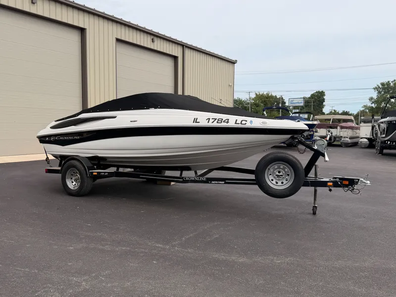 Slide: The Image of A 2009 Crownline 185 SS boat on a trailer, covered, parked in front of a building. - 1