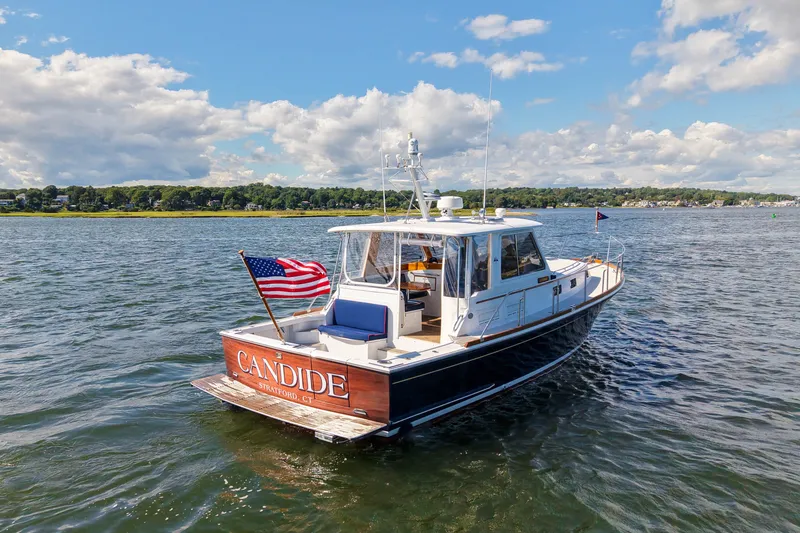 Slide: The Image of 2003 Grand Banks 38 Eastbay HX yacht on water, displaying American flag, clear sky background. - 2