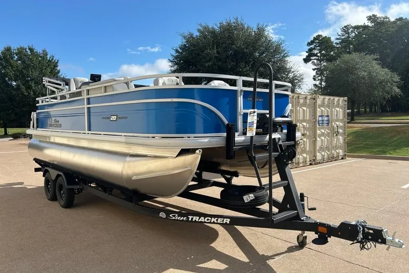 The Image of 2027 Sun Tracker Fishin' Barge 20 DLX pontoon boat on trailer, parked outdoors. - 0