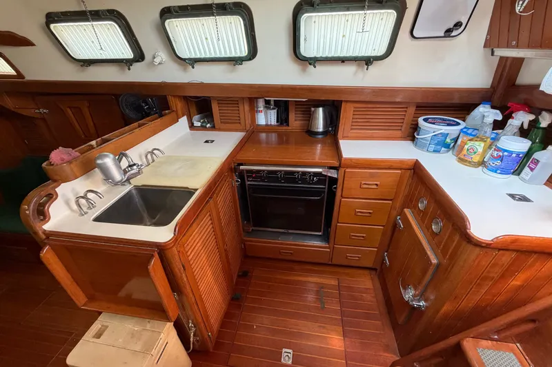 Slide: The Image of 1984 Tayana Aft Cockpit yacht kitchen with wooden cabinetry, sink, stove, and cleaning supplies. - 10