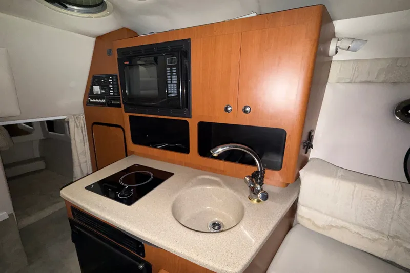 Slide: The Image of 2005 Crownline 270 CR boat interior with kitchenette, featuring sink, stove, and microwave. - 39