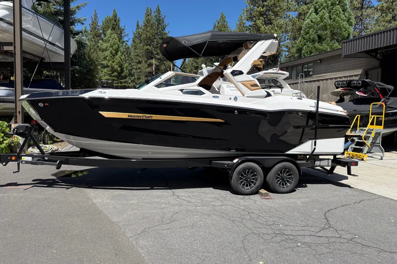 The Image of 2027 MasterCraft X24 boat on trailer, parked outdoors with trees in background. - 0