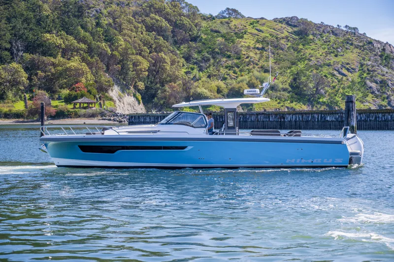 Slide: The Image of 2023 Nimbus Tender 11 boat cruising on scenic waterway with lush green hills. - 7