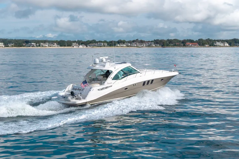 Slide: The Image of 2006 Sea Ray 48 Sundancer cruising on open water with scenic shoreline backdrop. - 4