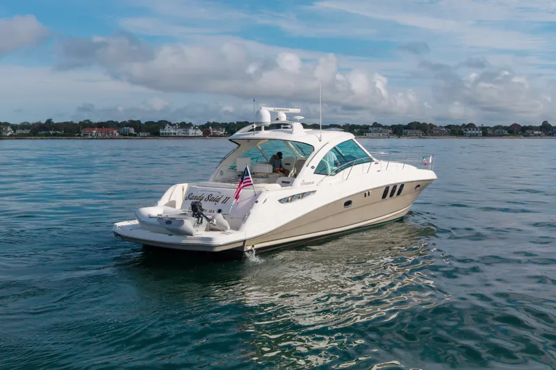 Slide: The Image of 2006 Sea Ray 48 Sundancer yacht cruising on calm waters near a coastal town. - 18