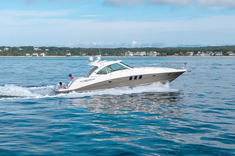 Slide: The Image of 2006 Sea Ray 48 Sundancer yacht cruising on calm waters near a coastal town. - 2